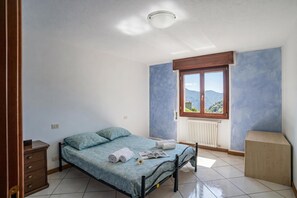 A bedroom with a bed, a window with a view, a radiator, and a wooden cabinet. - Balcone Di Alex & Thomas (Val Rezzo)