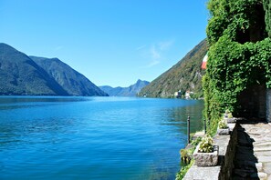 A calm lake with mountains in the background and a stone pathway with planters on the right. - Balcone Di Alex & Thomas (Val Rezzo)