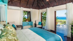A bedroom with a bed, a desk, a chair, and a view of the ocean. - Half Hill 1BR (Montego Bay)