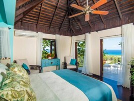 A bedroom with a bed, a desk, a chair, and a view of the ocean.