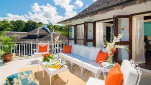 A sunlit outdoor seating area with a sofa, chairs, and a table set with flowers and a drink. - Half Hill 1BR (Montego Bay)