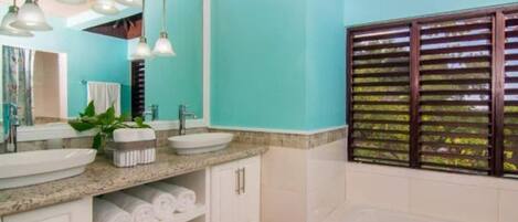 A bathroom with two sinks, a bathtub, and a window with blinds.