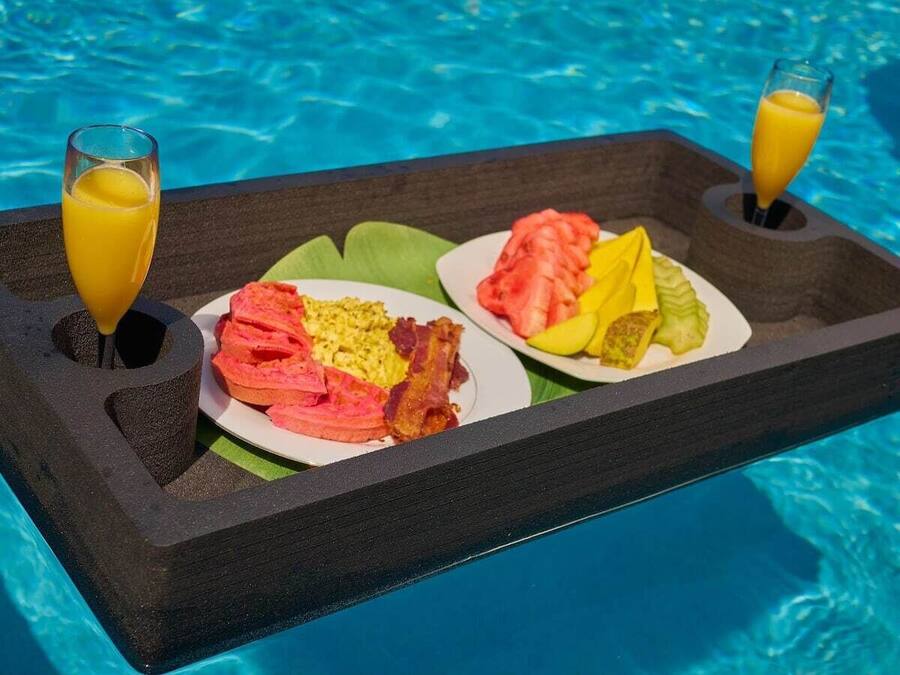 A breakfast tray with eggs, bacon, tomatoes, and a glass of orange juice by a pool.