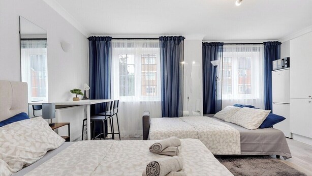 Habitación de hotel con dos camas, un escritorio, una silla, un radiador y vistas a la ciudad.