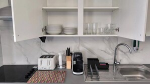 Una cocina con armarios blancos, encimera negra, una cafetera Bosch, un tostador, un lavabo y un bloque para cuchillos.