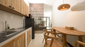 A modern kitchen with wooden cabinets, a black countertop, and a dining area with a wooden table and chairs. - Green Garden Villa Hotel (Rawai)