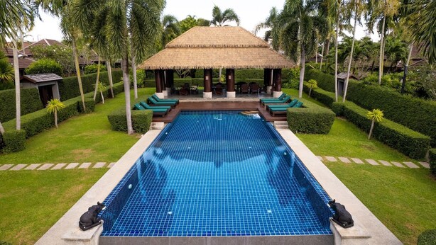 A rectangular swimming pool with a tiled surface, surrounded by well-manicured lawns and palm trees. - Green Garden Villa Hotel (Rawai)