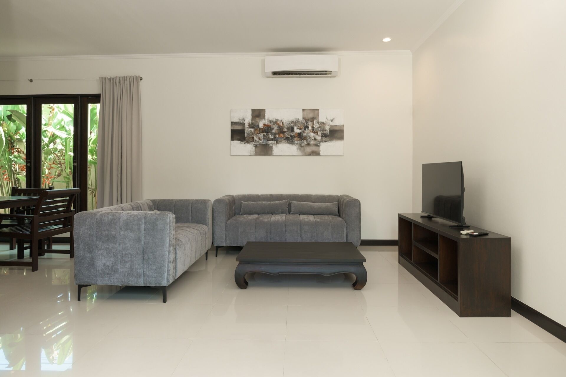A modern living room with a grey sofa, a coffee table, a TV on a stand, and a dining area with a table and chairs.
