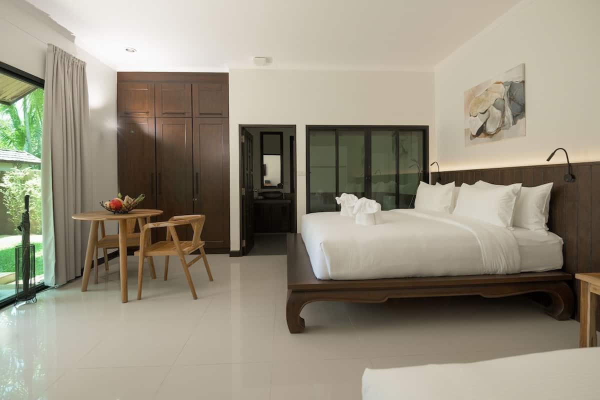 A modern hotel room with a large bed, a dining area with a table and chairs, and a view of the outdoors.