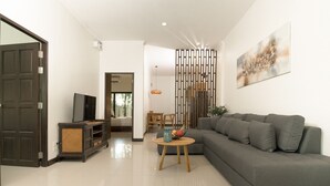 A modern living room with a grey sofa, a wooden coffee table, and a television on a stand. - Green Garden Villa Hotel (Rawai)