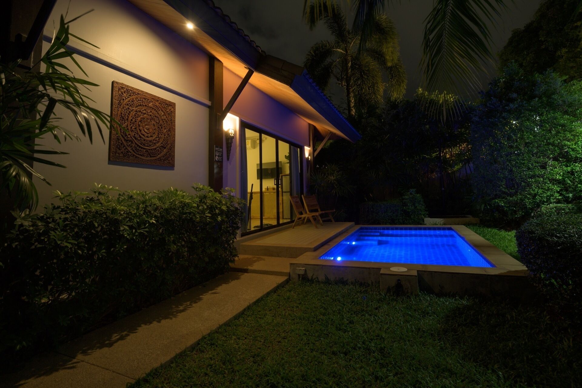 A modern house with a swimming pool, surrounded by lush greenery and palm trees.