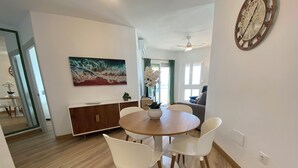 Uma sala de jantar com uma mesa redonda de madeira, cadeiras brancas, um armário de madeira e um quadro na parede.
