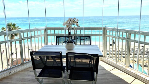 Varanda com mesa e cadeiras, vista para a praia e o oceano.