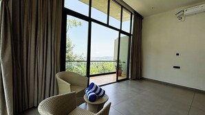 Une pièce spacieuse dotée d’une grande porte-fenêtre coulissante qui donne sur un balcon offrant une vue sur la verdure et un paysage lointain.