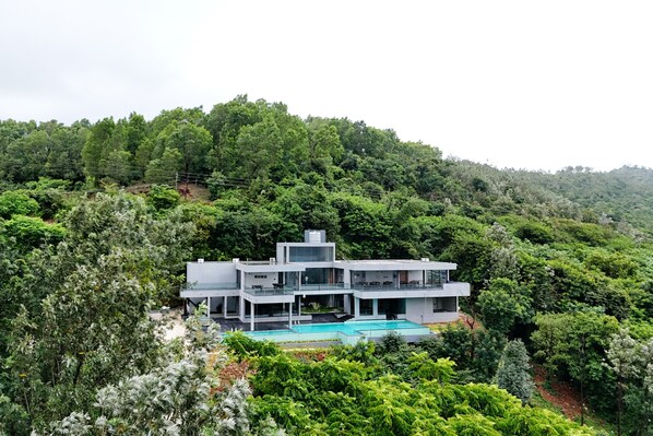 Ein modernes, zweistöckiges Haus mit Schwimmbecken, umgeben von dichtem Wald.