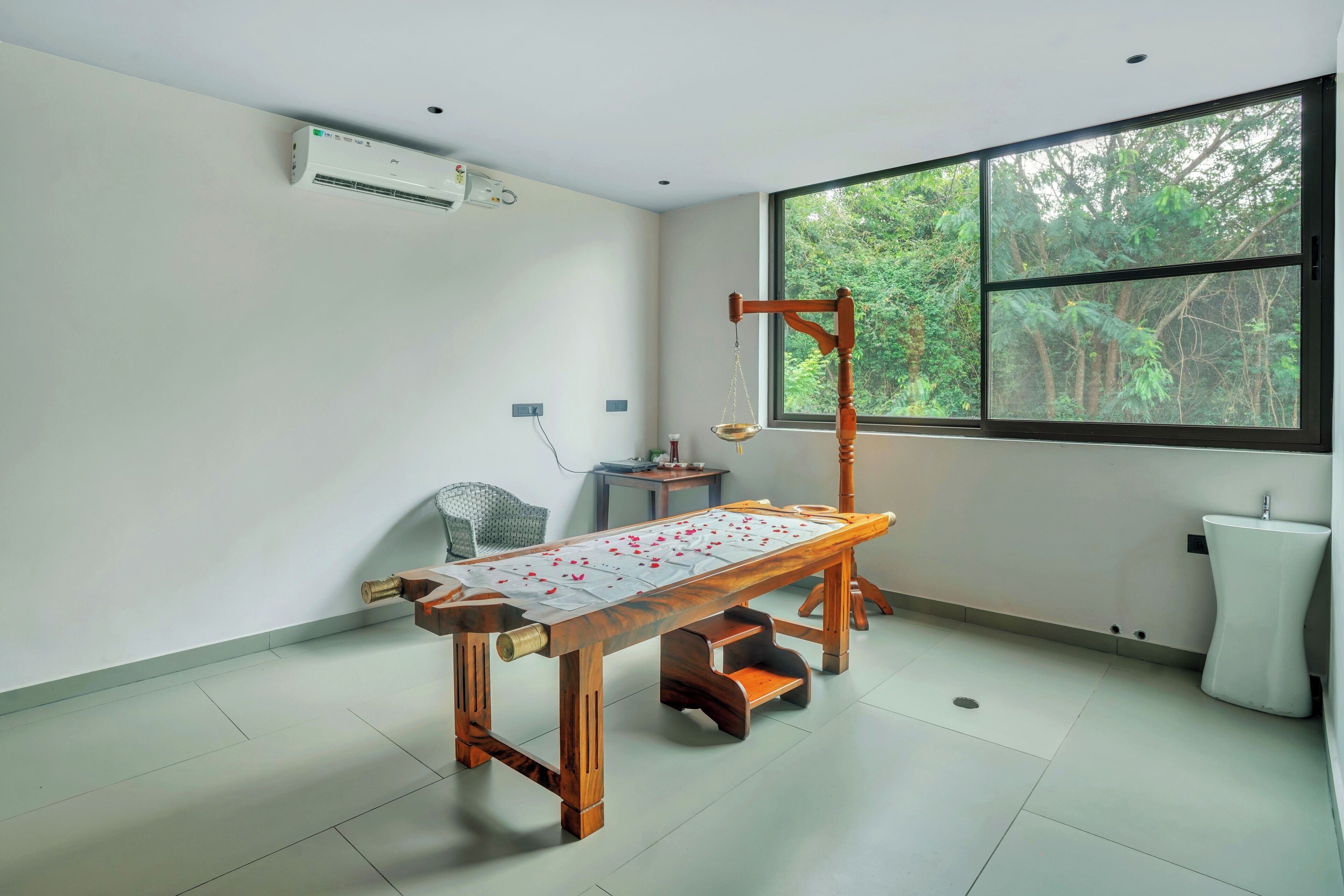 Een kamer met een tafel met tatami-matten, een houten stoel, een raam met uitzicht op bomen en een witte airconditioningunit aan de muur.