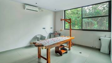 A room with a tatami mat table, a wooden chair, a window with a view of trees, and a white air conditioning unit on the wall.