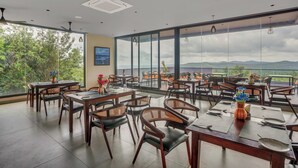 Un vaste espace dédié à la salle à manger, avec de nombreuses tables et chaises, de grandes fenêtres offrant une vue sur l’extérieur et des ventilateurs de plafond.