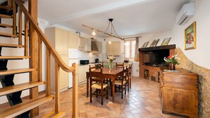 A spacious kitchen with a wooden staircase, a dining area with chairs, and a fireplace.