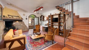 A cozy living room with a fireplace, comfortable seating, a staircase, and a kitchen area.
