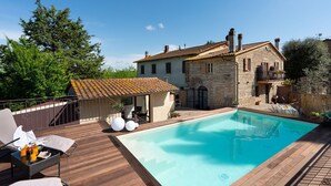A stone house with a swimming pool, a covered patio, and a wooden deck.