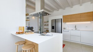 Una cocina moderna con una isla central, taburetes de bar, una campana extractora de acero inoxidable y armarios de madera.