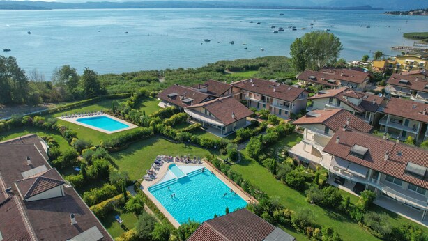 Una zona residencial con dos piscinas rodeadas de abundante vegetación y casas con techos de tejas rojas.