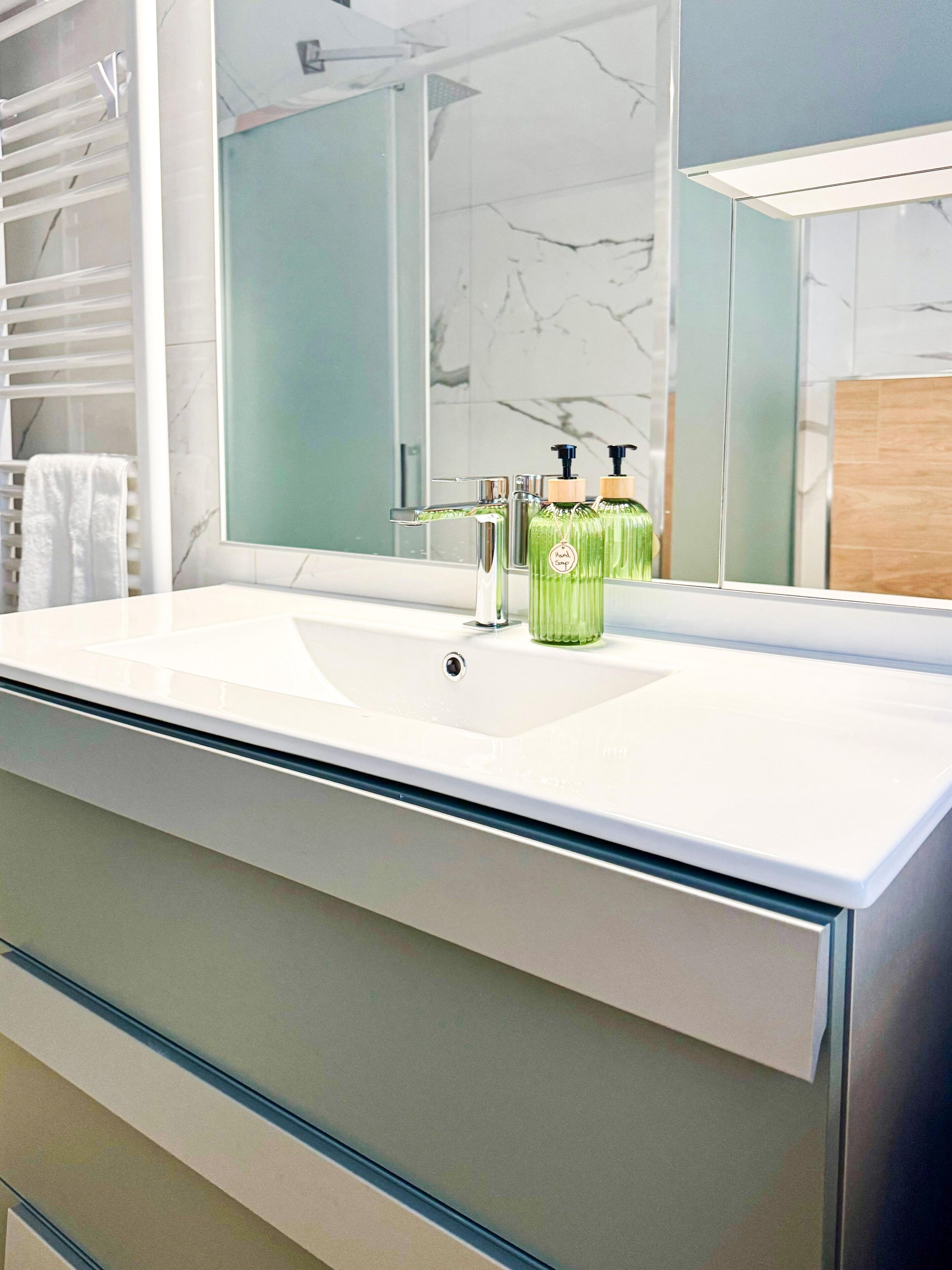 A bathroom with a white sink, a mirror, and two green soap dispensers.