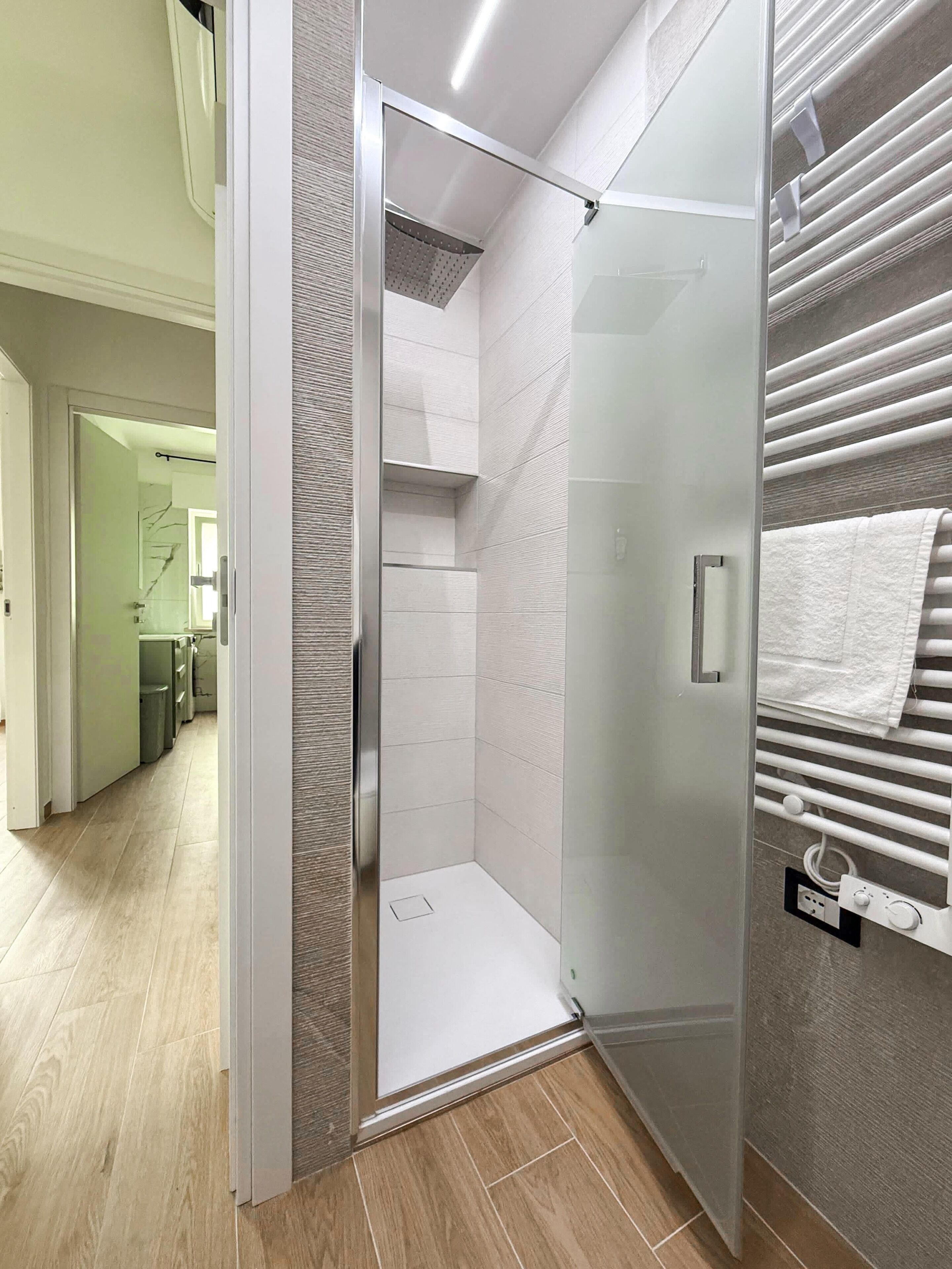 Ein modernes Badezimmer mit einer gläsernen Duschkabine, einem Handtuchhalter und einer sichtbaren Toilette.