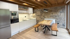 Una cocina moderna con armarios blancos, horno empotrado, pared de piedra y una mesa de comedor de madera con bancos.