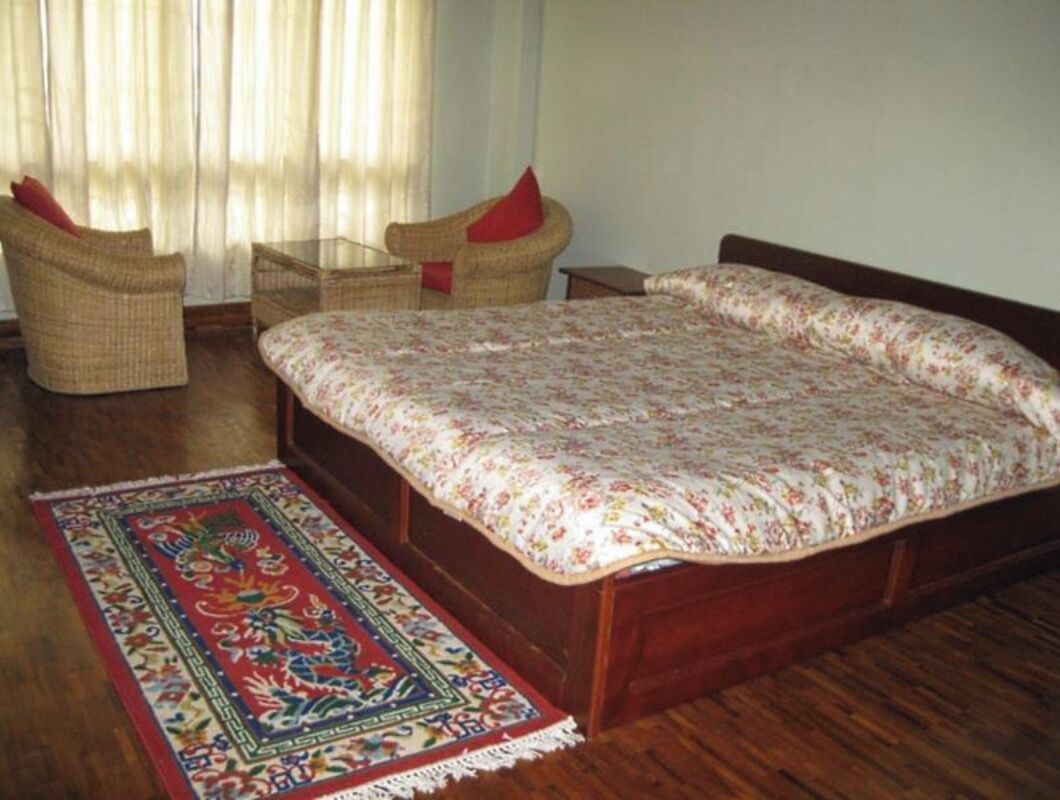A bedroom with a wooden bed, a woven chair, a small table, and a patterned rug.