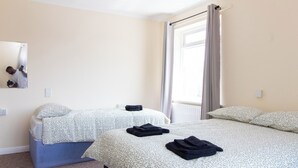 A hotel room with two beds, a window with curtains, a mirror on the wall, and a small bedside table. - Brookvale Guest House Room 12 (Southampton)