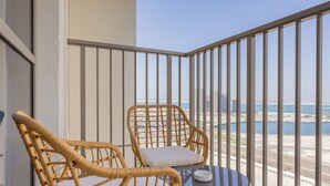 Ein Balkon mit Korbstühlen und einem kleinen Tisch, der Blick auf die Küste mit Gebäuden und Wasser freigibt.