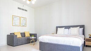 Ein modernes Schlafzimmer mit einem grauen Sofa, einem Bett mit weißer Bettwäsche und zwei gerahmten Kunstwerken an der Wand.