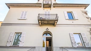 Un bâtiment à deux étages doté d’un balcon, de volets et d’une entrée centrale surmontée d’une arche.