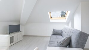 Un salon moderne et minimaliste, doté d’un plafond en pente et d’une lucarne.