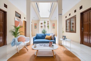Una sala de estar moderna con un sofá azul, una mesa de centro blanca y un sillón mecededor. Hay un tragaluz arriba y el piso es de madera.
