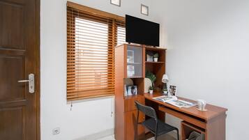 Una habitación con un escritorio de madera, una silla, un televisor montado en la pared y una ventana con persianas.