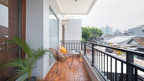 A balcony with a wooden floor, two wicker chairs with cushions, a small table, and a potted plant.
