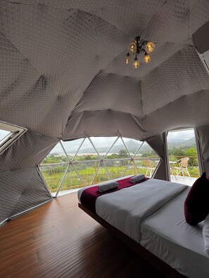 A bedroom with a large window, a bed, and a view of a green landscape. - Sova's Nature Hideout (Mawal)