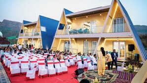 Una gran multitud en un espacio al aire libre con asientos escalonados y un escenario, rodeado por un edificio de diseño triangular distintivo.