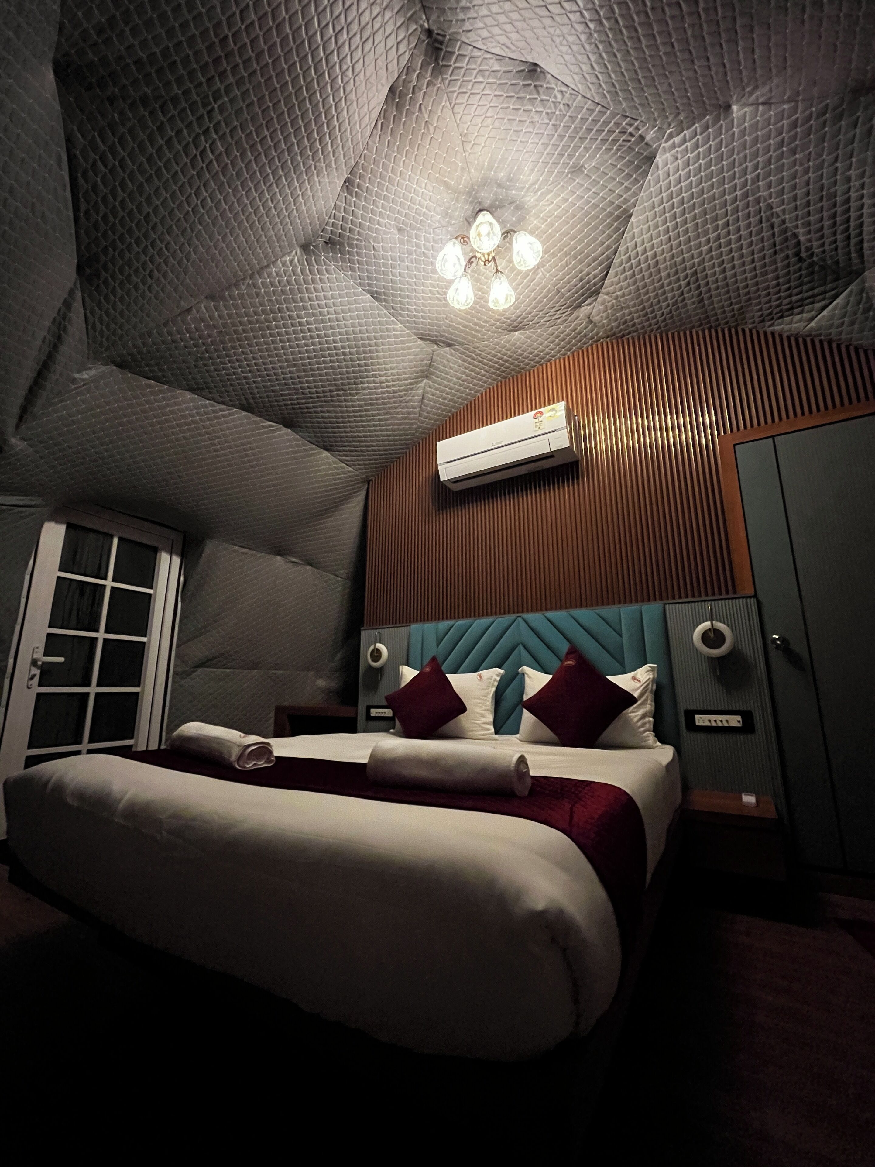 Ein Schlafzimmer mit einem Bett, einer Klimaanlage, einer Tür und einer Wandleuchte.
