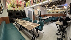 Un restaurante con asientos y mesas color turquesa, decoraciones florales colgantes y un ventilador a la derecha.