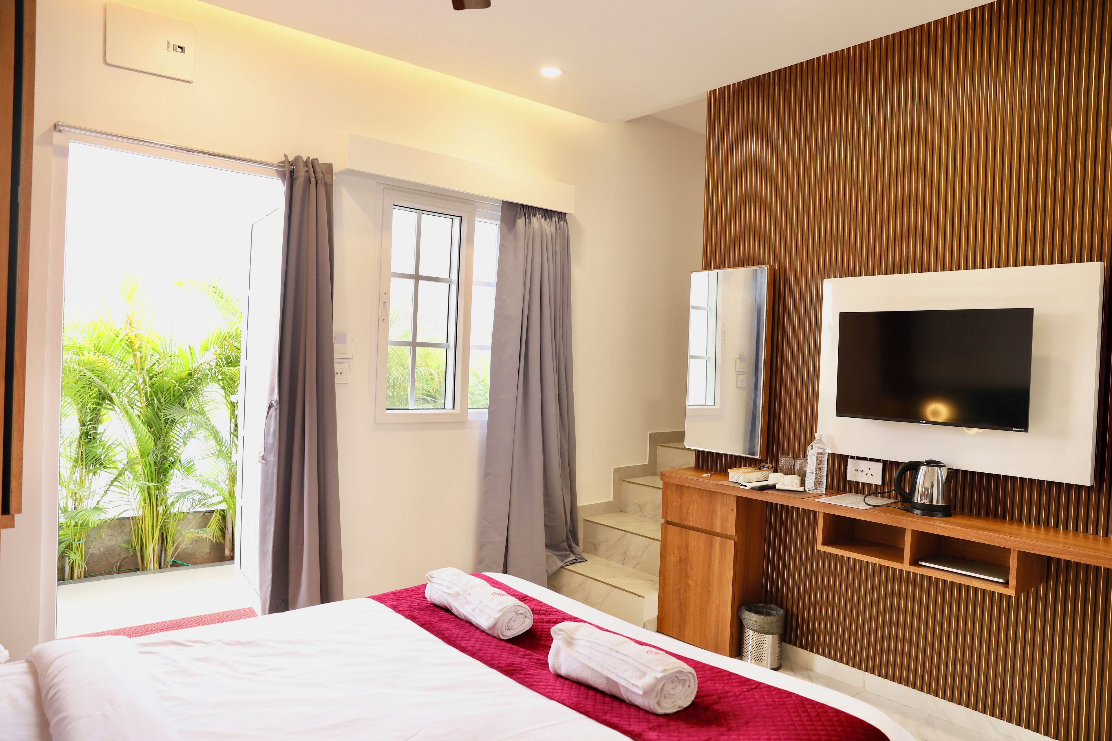A hotel room with a bed, a TV, a wooden panel wall, and a window with curtains.