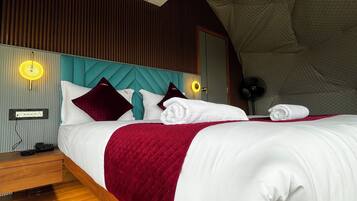Un dormitorio moderno con suelo de madera, una cama grande con ropa de cama blanca y burdeos, un cabecero verde azulado y un diseño de techo único.