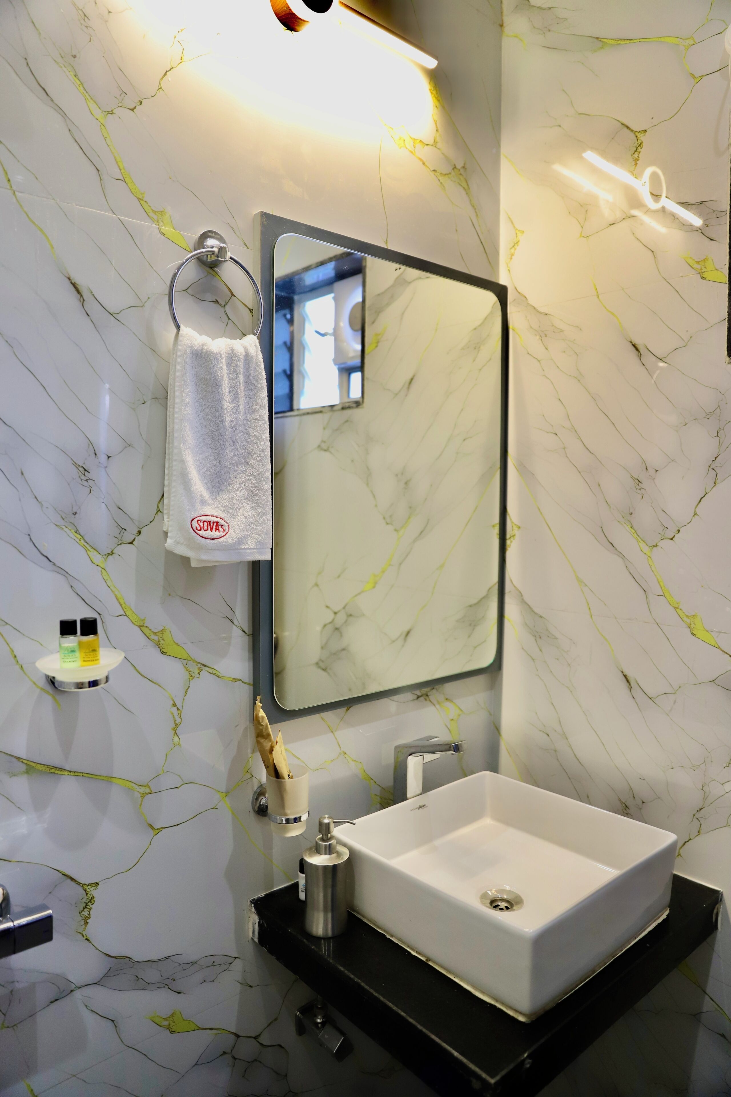 Un baño con salpicadero de mármol blanco, un lavabo blanco, un espejo y una toalla colgada en un aro metálico.