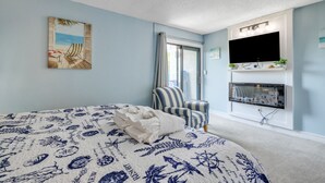 Un dormitorio con cama, un sillón a rayas, televisión y ventana con cortinas.