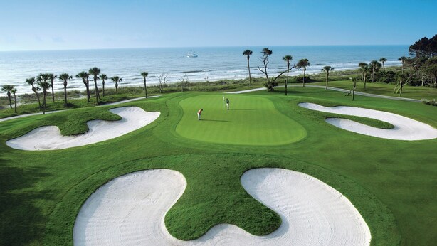Un campo de golf con búnkeres de arena, palmeras y vistas al océano.