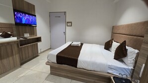 Ein Hotelzimmer mit Bett, Fernseher, Holz-Kopfteil und Nachttisch.