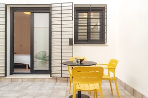 A room with a bed, a sliding glass door, a small table with two yellow chairs, and a window with black blinds. - Los Olivos Apartments by Olala Homes  (Seville)